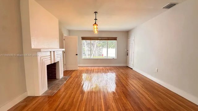 an empty room with wooden floor a fireplace and windows