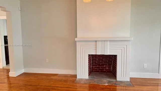 a view of an empty room with wooden floor and a fireplace