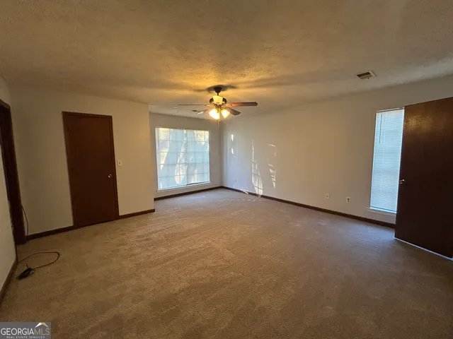 an empty room with a chandelier fan and windows