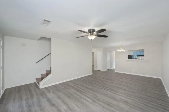 a view of an empty room with wooden floor and a ceiling fan