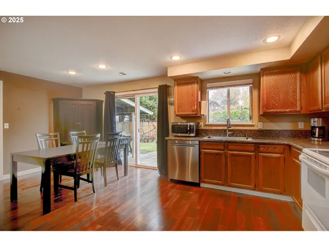 a kitchen with stainless steel appliances granite countertop a refrigerator a sink dishwasher a stove and a dining table with wooden floor