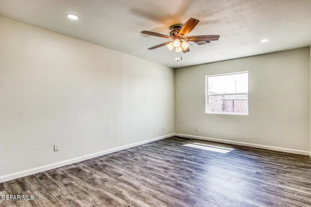 an empty room with wooden floor fan and windows