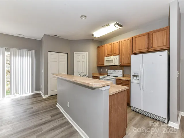 a kitchen with stainless steel appliances granite countertop a refrigerator a sink dishwasher a stove and white countertops with wooden floor