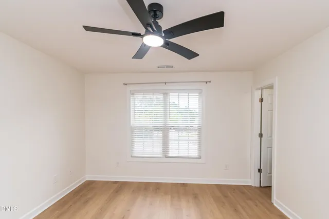 an empty room with wooden floor ceiling fan and windows