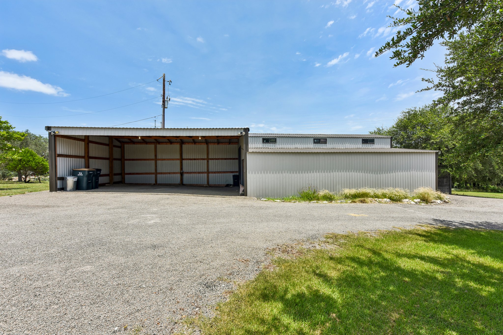 2203 Improver Road Spicewood, TX 78669 - Photo 26 of 38 A spacious gravel parking area extends before a large, metal-sided storage or workshop facility.