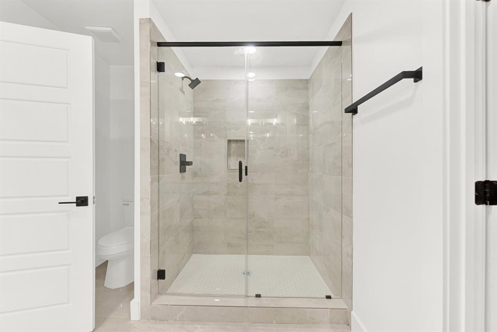 9471 Timberleaf Drive Dallas, TX 75243 - Photo 31 of 39 Glass-enclosed shower featuring large format tile walls, a built-in shower niche, and matte black fixtures