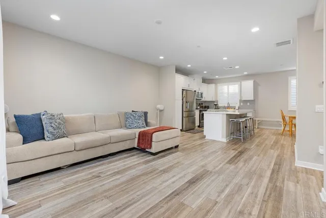 a living room with stainless steel appliances furniture wooden floor and a kitchen view