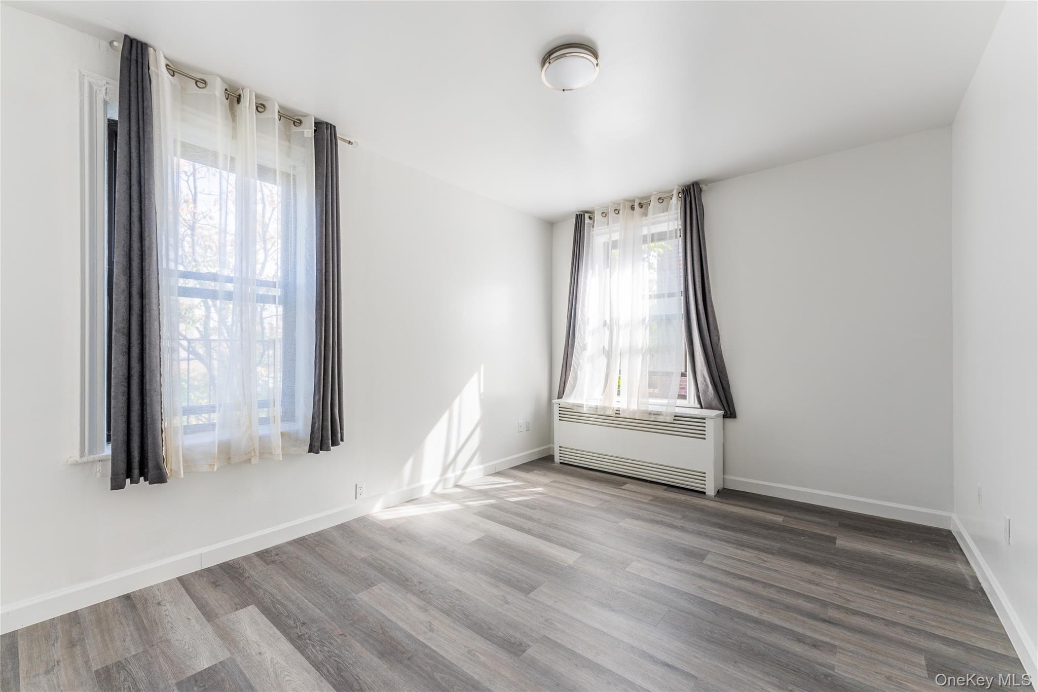 136-05 Sanford Avenue, Unit 6S Queens, NY 11355 - Photo 11 of 15 an empty room with wooden floor and windows