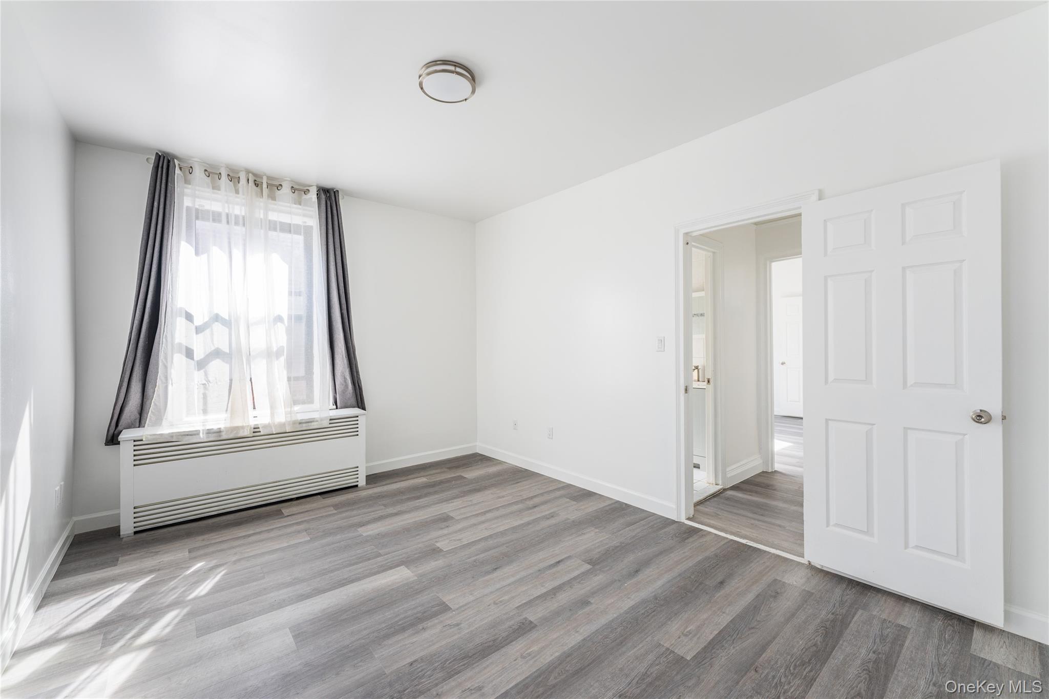 136-05 Sanford Avenue, Unit 6S Queens, NY 11355 - Photo 12 of 15 an empty room with wooden floor and windows