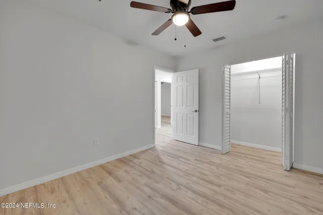 an empty room with wooden floor chandelier fan and windows