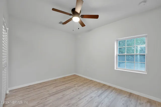 an empty room with wooden floor ceiling fan and windows