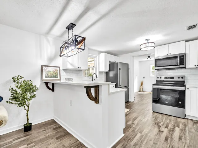 a kitchen with stainless steel appliances granite countertop a refrigerator a stove a microwave oven a sink dishwasher and white cabinets with wooden floor