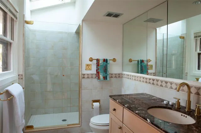a bathroom with a granite countertop sink a toilet a mirror and shower