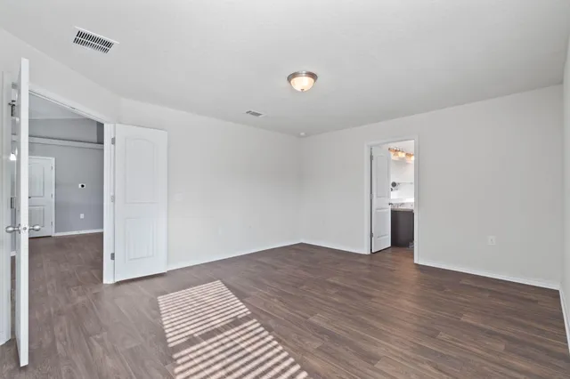 a view of an empty room with wooden floor and a bathroom
