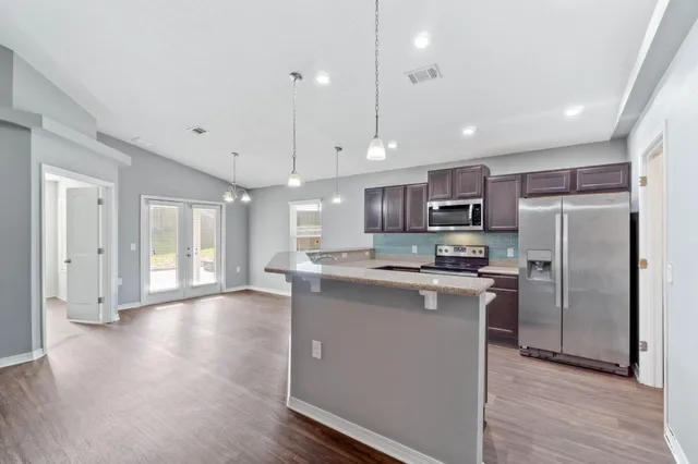 a kitchen with stainless steel appliances granite countertop a refrigerator a sink dishwasher a stove and white cabinets with wooden floor