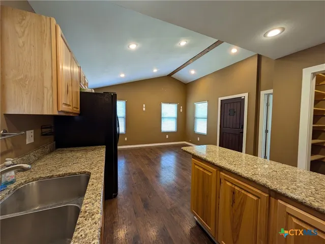 a kitchen with stainless steel appliances granite countertop a refrigerator a sink dishwasher and wooden cabinets with wooden floor