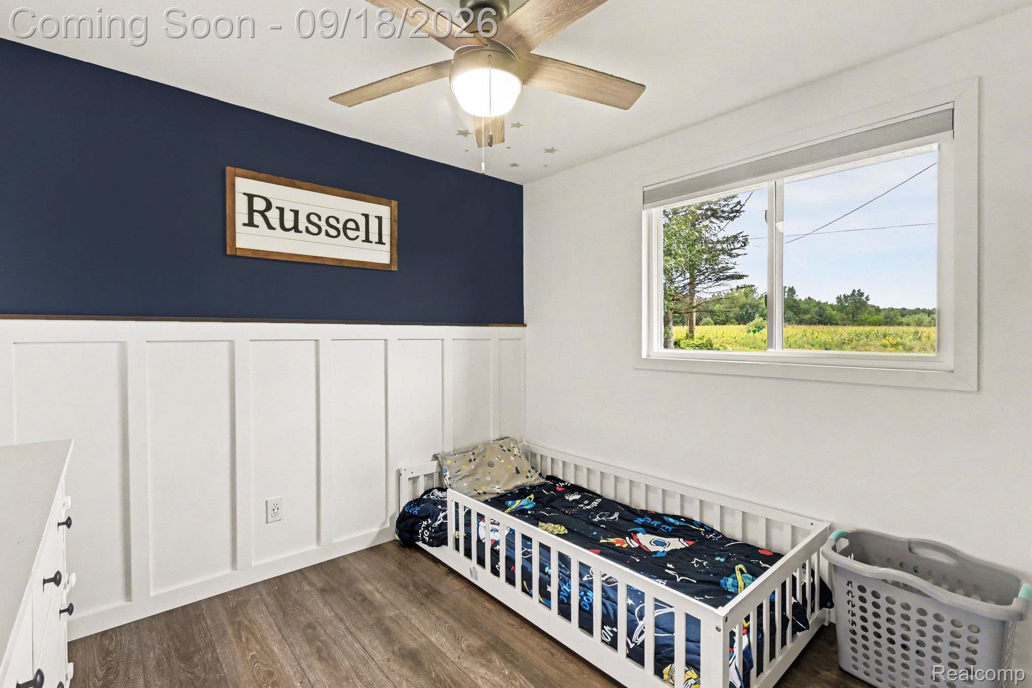 10755 Spencer Road St. Charles, MI 48655 - Photo 21 of 35 Wood-finish flooring, white board and batten wainscoting, a contrasting accent wall, a ceiling fan with integrated lighting, and a window with white trim
