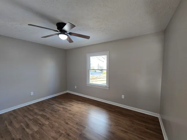 an empty room with wooden floor fan and windows