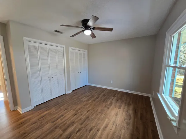 an empty room with wooden floor fan and windows