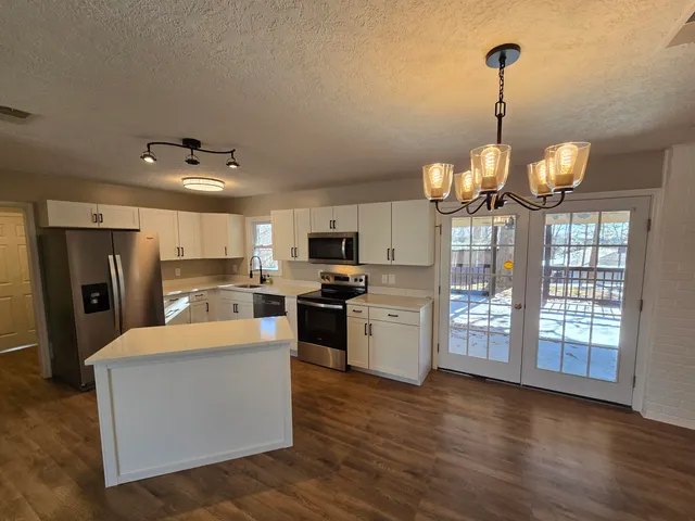 a kitchen with stainless steel appliances granite countertop a refrigerator a sink dishwasher a stove and white countertops with wooden floor