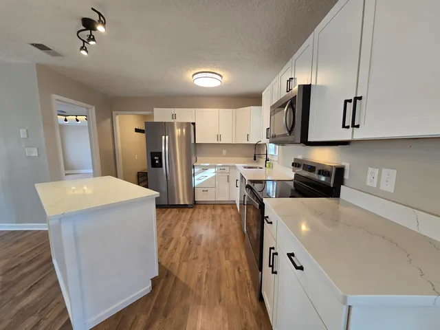 a kitchen with stainless steel appliances granite countertop a refrigerator a sink dishwasher a stove and white countertops with wooden floor