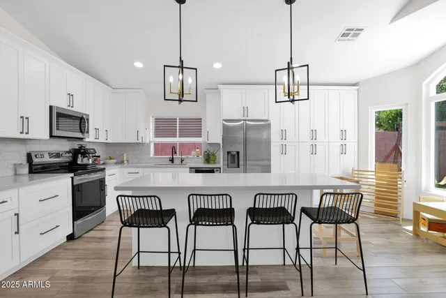 a kitchen with stainless steel appliances kitchen island granite countertop a dining table chairs refrigerator and microwave