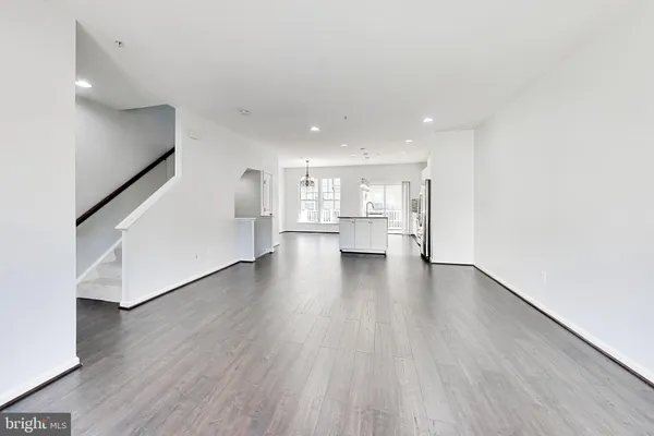 a view of empty room with wooden floor and kitchen