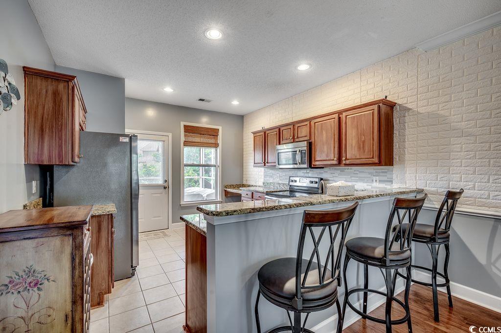 100 Culpepper Way, Unit 1002 Myrtle Beach, SC 29579 - Photo 7 of 39 Kitchen with appliances with stainless steel finishes, a peninsula, a textured ceiling, stone counters, and brown cabinetry