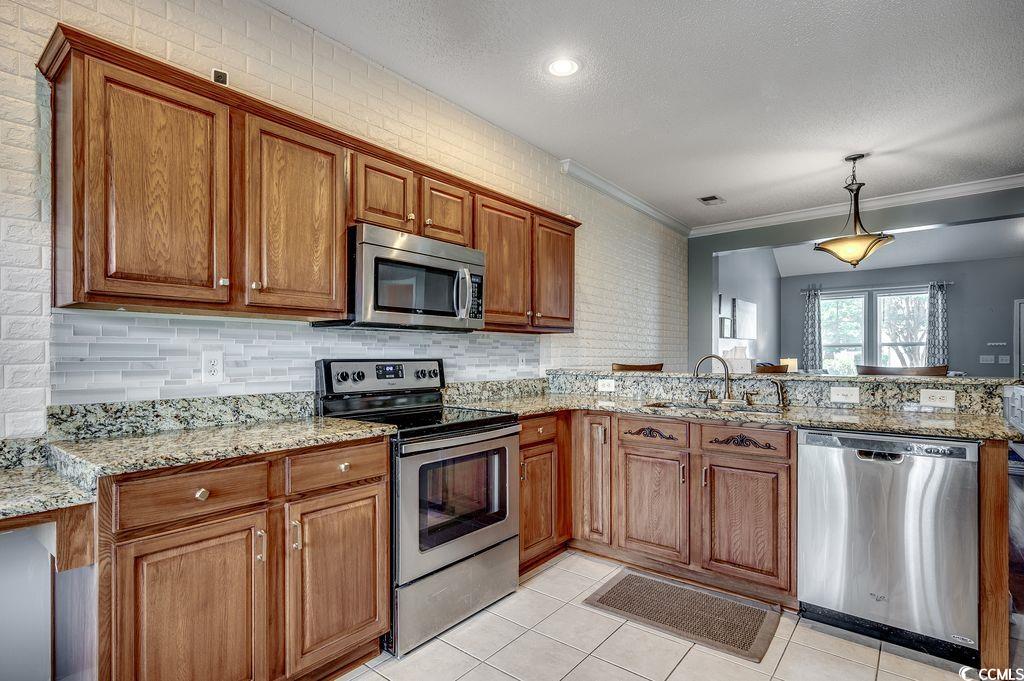 100 Culpepper Way, Unit 1002 Myrtle Beach, SC 29579 - Photo 8 of 39 Kitchen featuring appliances with stainless steel finishes, brown cabinetry, a peninsula, light tile patterned floors, and crown molding