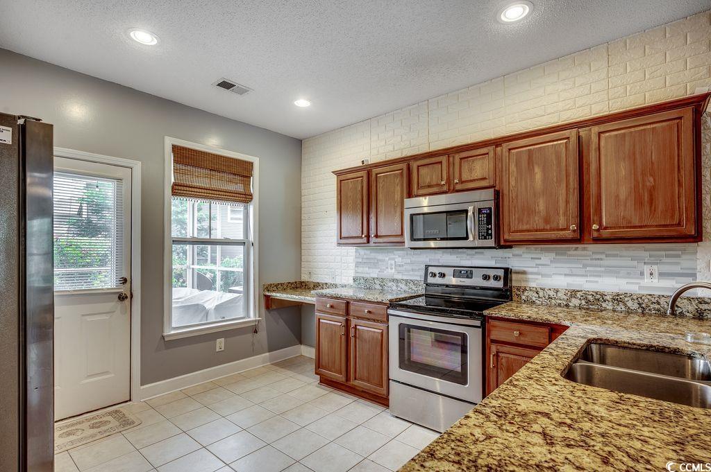 100 Culpepper Way, Unit 1002 Myrtle Beach, SC 29579 - Photo 9 of 39 Kitchen with stainless steel appliances, light tile patterned floors, a textured ceiling, backsplash, and light stone counters
