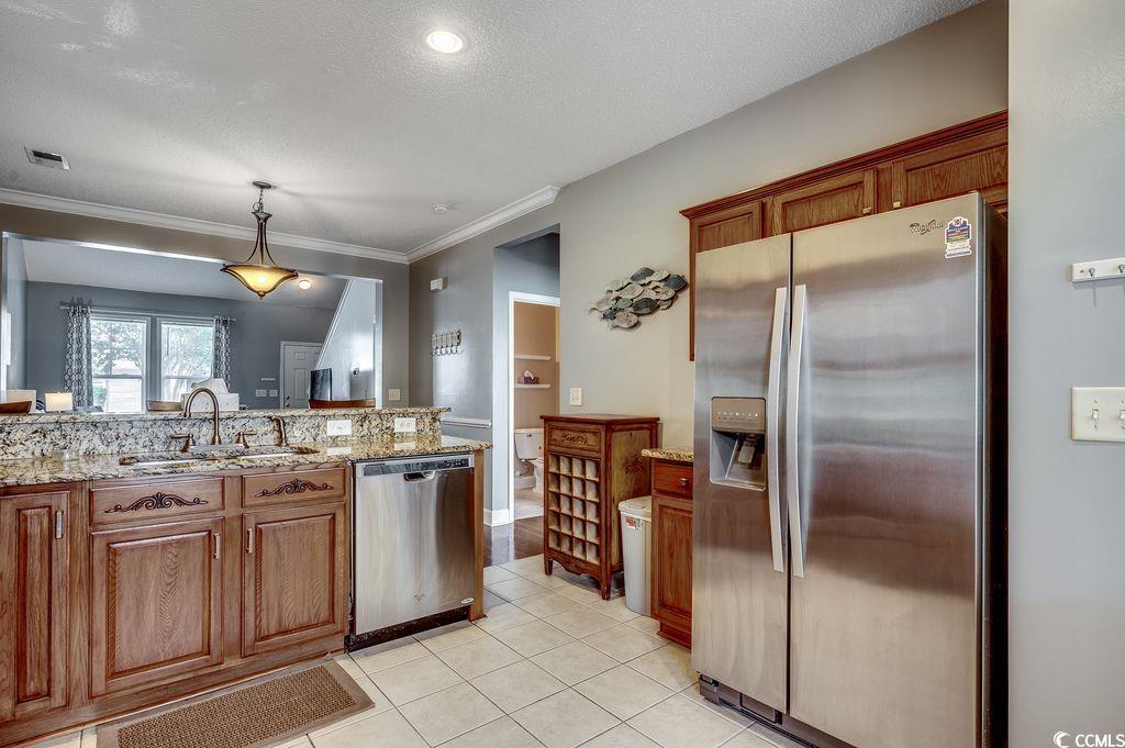 100 Culpepper Way, Unit 1002 Myrtle Beach, SC 29579 - Photo 10 of 39 Kitchen with appliances with stainless steel finishes, light tile patterned floors, brown cabinets, light stone countertops, and crown molding