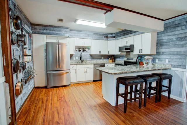 a kitchen with stainless steel appliances granite countertop a refrigerator a sink dishwasher a stove and a microwave oven with wooden floor