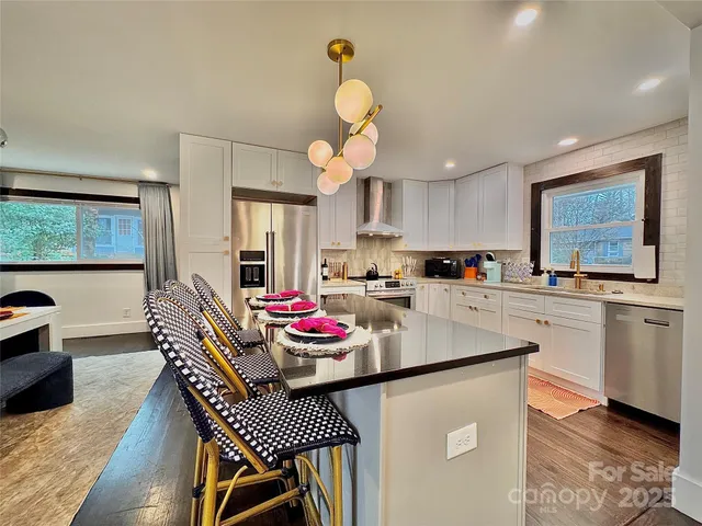 a kitchen with stainless steel appliances granite countertop a sink dishwasher a stove a dining table and chairs with wooden floor