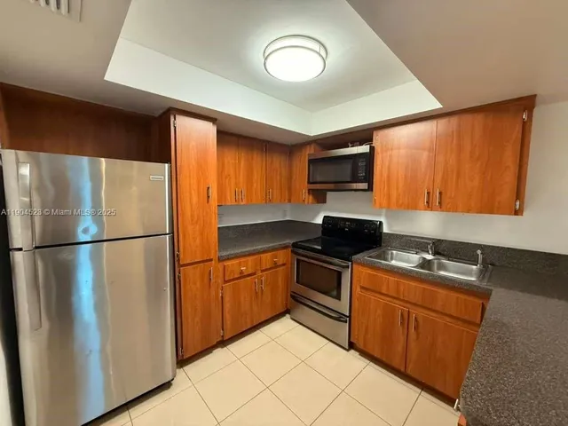 a kitchen with granite countertop a refrigerator a sink a stove top oven and cabinets