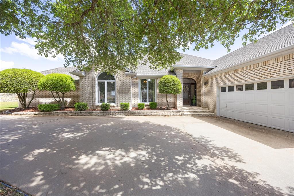 View of front of home with roof with shingles, concrete driveway, a garage, and brick siding