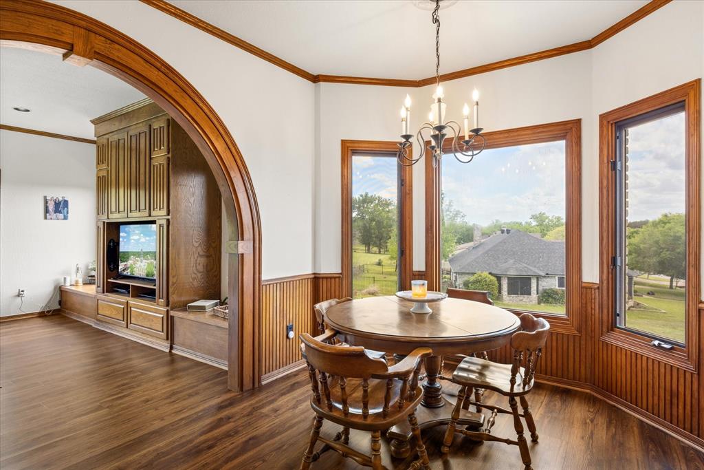 8911 Bontura Road Granbury, TX 76049 - Photo 12 of 39 Dining space featuring arched walkways, crown molding, a chandelier, dark wood-type flooring, and wainscoting
