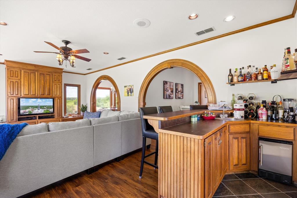 8911 Bontura Road Granbury, TX 76049 - Photo 16 of 39 Indoor wet bar featuring dark countertops, wood finish cabinetry, stainless steel refrigerator, recessed lighting, and crown molding