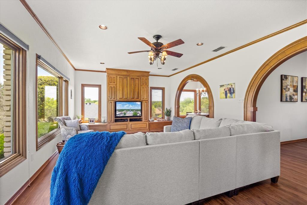 8911 Bontura Road Granbury, TX 76049 - Photo 17 of 39 Living room with ceiling fan, dark wood-style floors, crown molding, arched walkways, and a chandelier