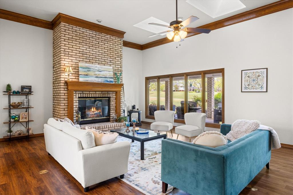 8911 Bontura Road Granbury, TX 76049 - Photo 3 of 39 Living area with crown molding, dark wood-style flooring, ceiling fan, and a brick fireplace