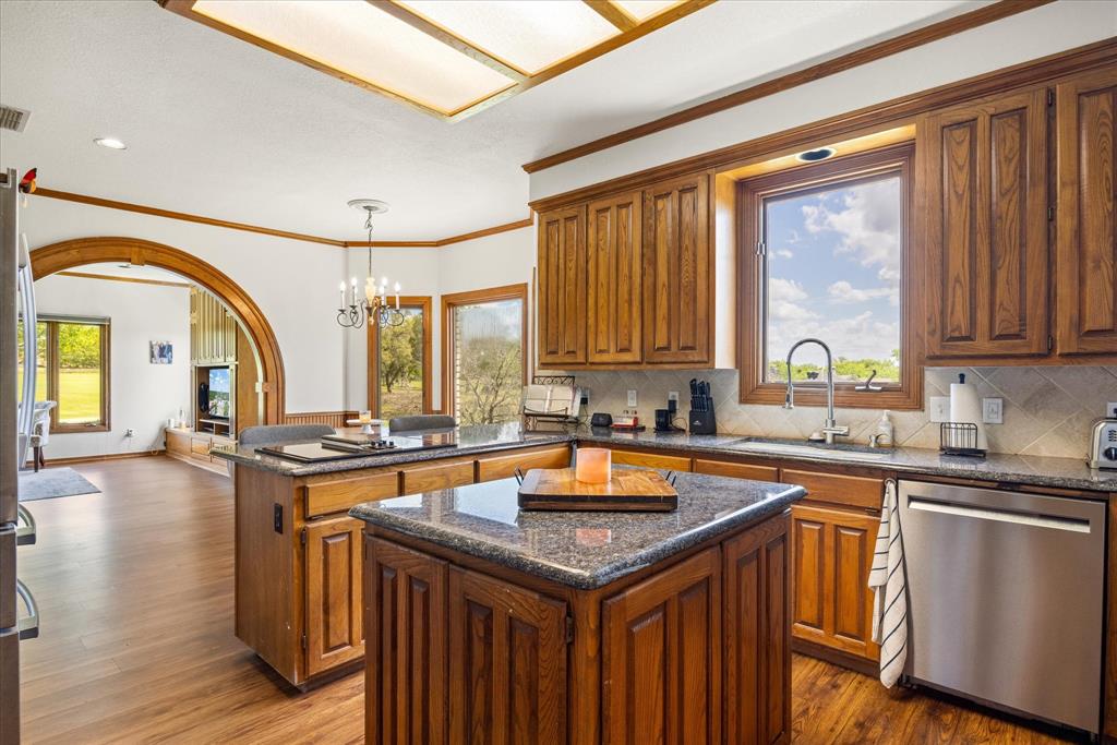 8911 Bontura Road Granbury, TX 76049 - Photo 9 of 39 Kitchen featuring a peninsula, wood finish cabinetry, stainless steel appliances, ornamental molding, and dark wood-style flooring