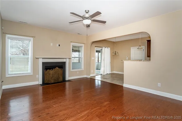 an empty room with wooden floor a ceiling fan and a kitchen view