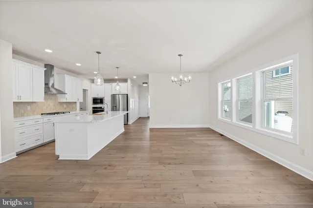 a large white kitchen with kitchen island a stove a sink a refrigerator and white cabinets with wooden floor