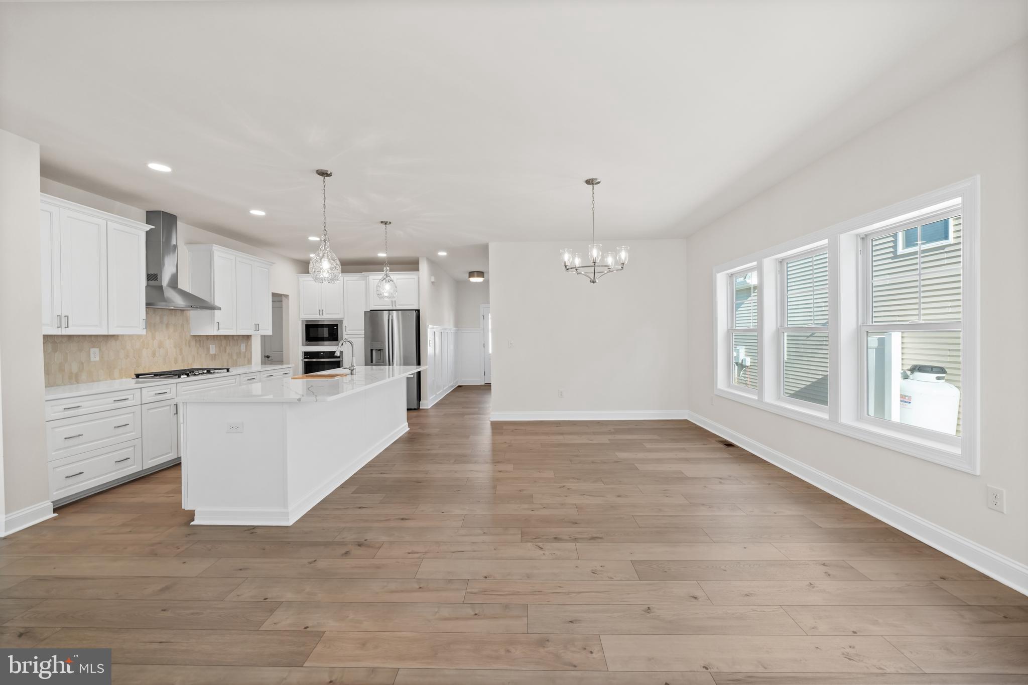 33766 Catching Cove Lewes, DE 19958 - Photo 15 of 47 a large white kitchen with kitchen island a stove a sink a refrigerator and white cabinets with wooden floor
