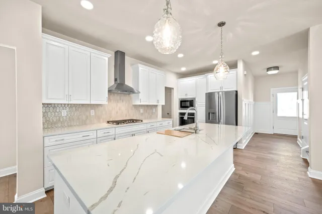 a large kitchen with stainless steel appliances kitchen island granite countertop a stove a refrigerator a oven and white cabinets with wooden floor