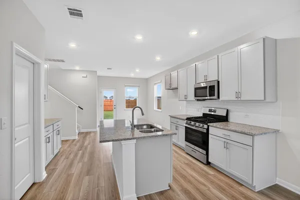 a kitchen with stainless steel appliances granite countertop a stove top oven a sink dishwasher a refrigerator and white cabinets with wooden floor