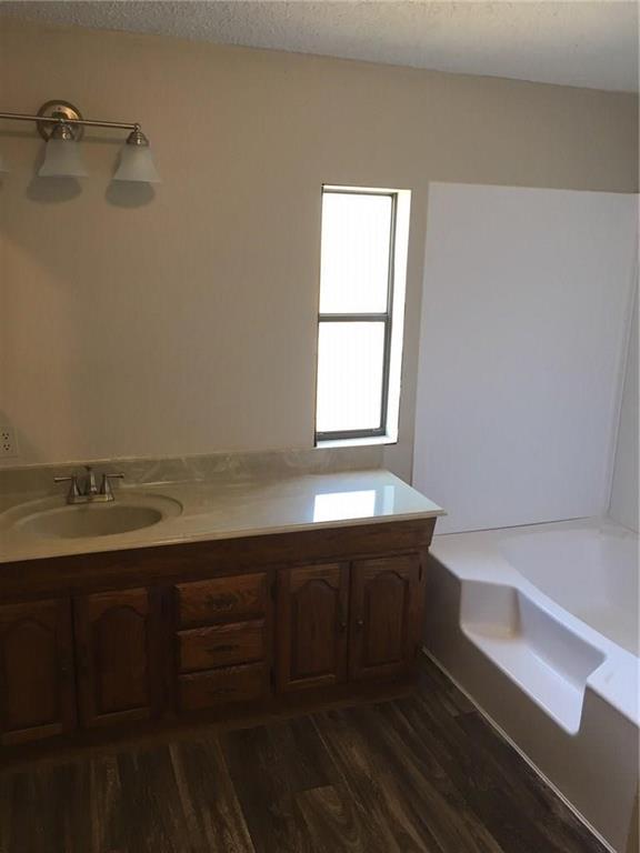365 Darrell Road Roanoke, TX 76262 - Photo 14 of 22 Wood-finish flooring, wood vanity with integrated sink, light countertop, three-light vanity fixture, and a built-in tub