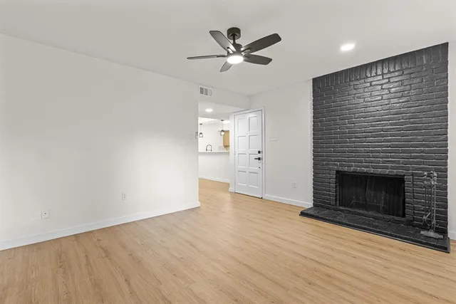 an empty room with wooden floor a ceiling fan a fireplace and windows