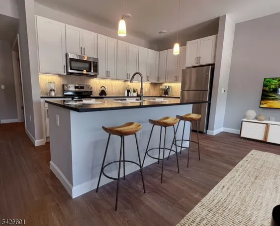 a kitchen with stainless steel appliances granite countertop a microwave a stove a sink a refrigerator and white cabinets with wooden floor