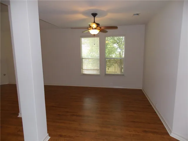 an empty room with wooden floor chandelier fan and windows