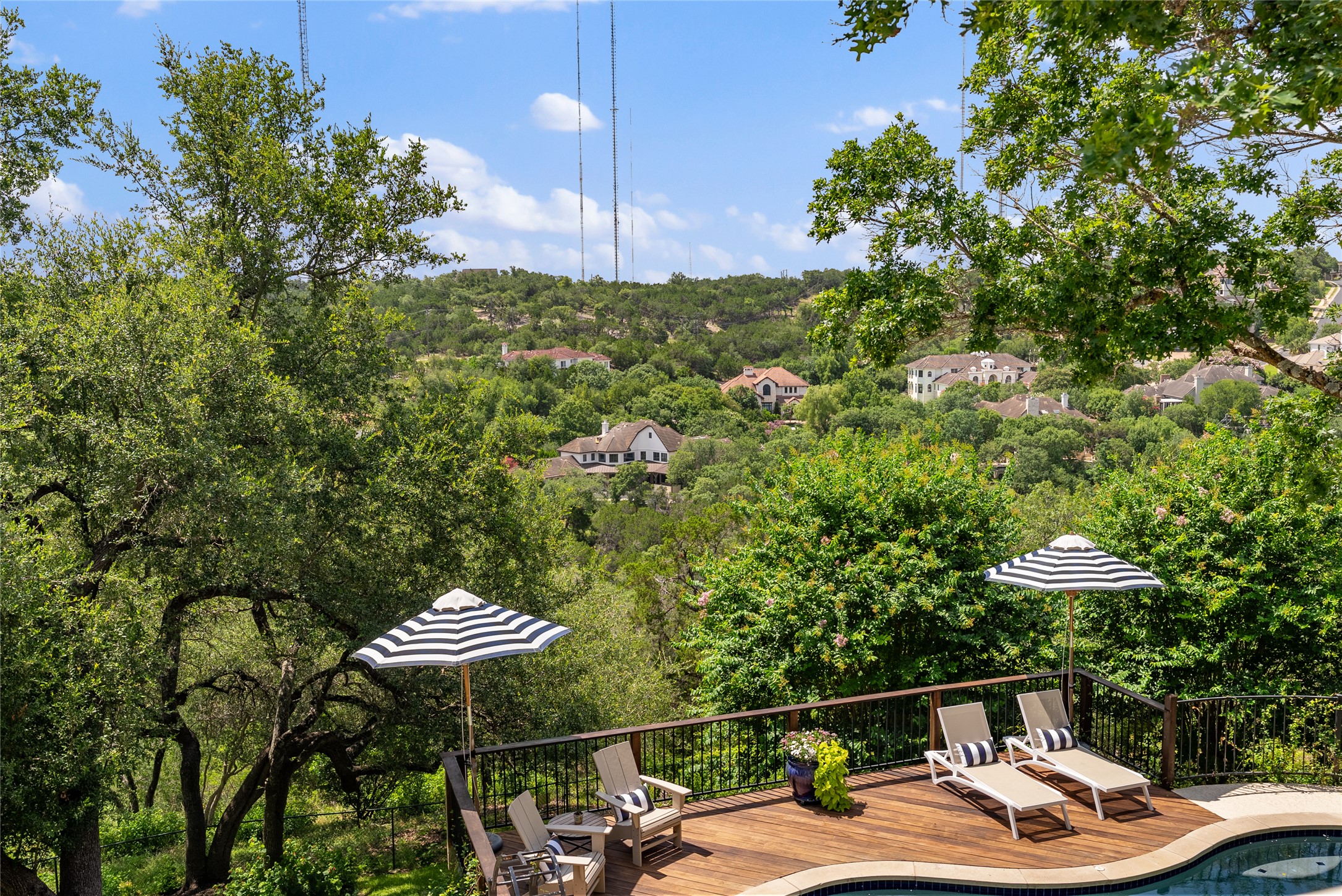 3107 Lookout Lane Austin, TX 78746 - Photo 16 of 39 An inviting pool and deck area overlooks a verdant hillside with distant homes under a vast sky.